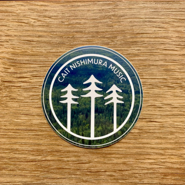 Cait Nishimura Music circle shaped sticker with white logo over forest photograph